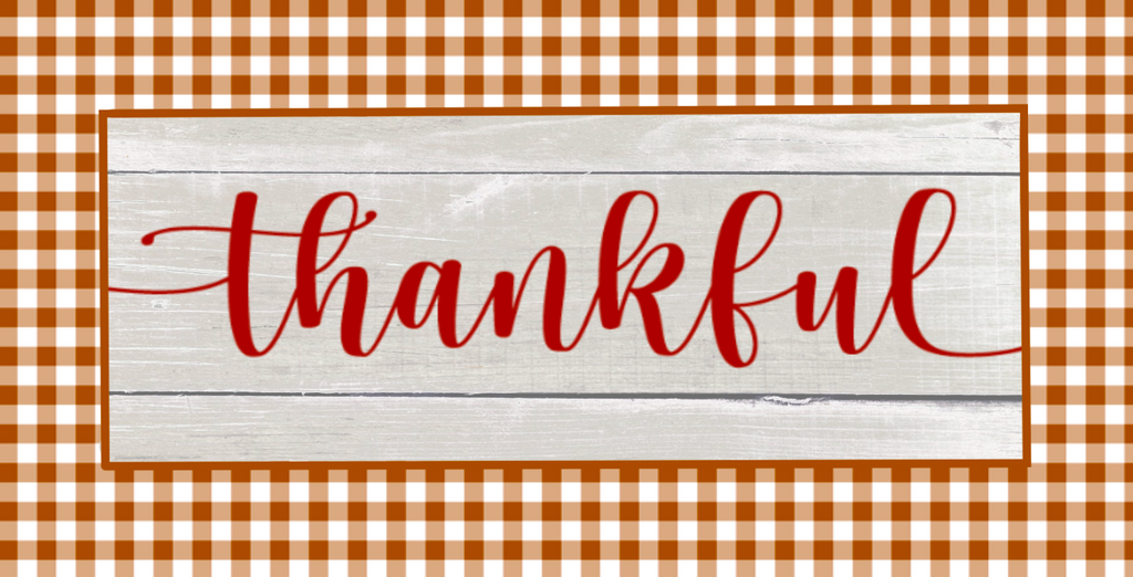 12 inch metal wreath sign with Thankful printed in burgundy atop an aged wood background and surrounded by a brown and tan gingham pattern.