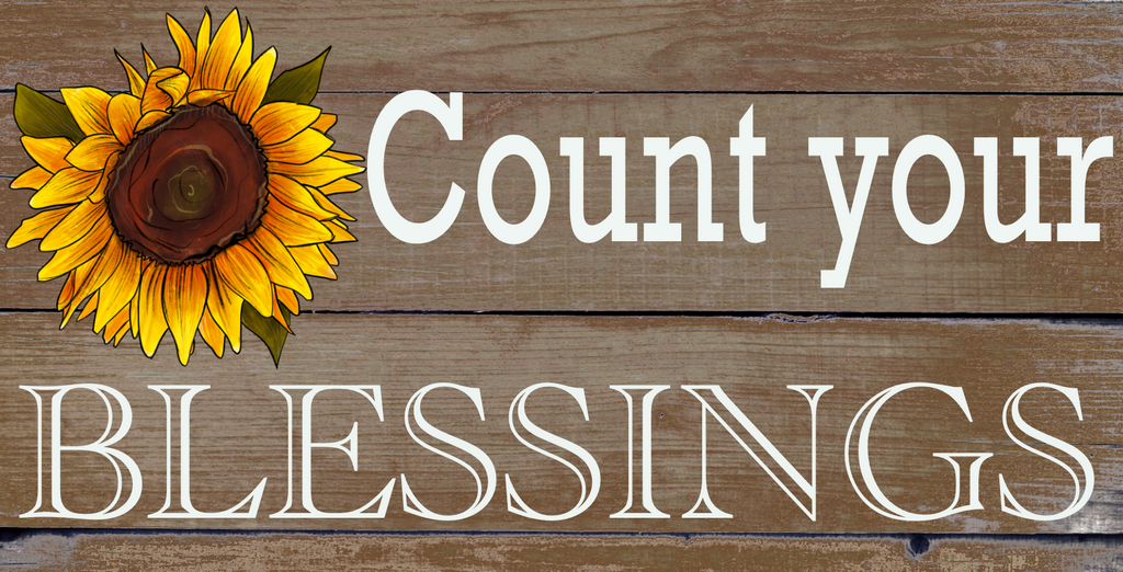 12 inch metal wreath sign with count your blessings printed in white atop an aged wood background and accented with a single sunflower bloom