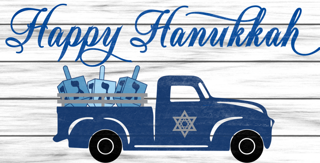 Happy Hanukkah is written in dark blue against a white shiplap background and features an antique blue truck full of dreidel's.